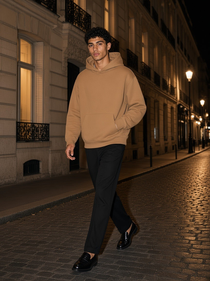 Man in the Essential Heavyweight Hoodie, 400 gsm in Camel walking down a Haussmann street in Paris at night