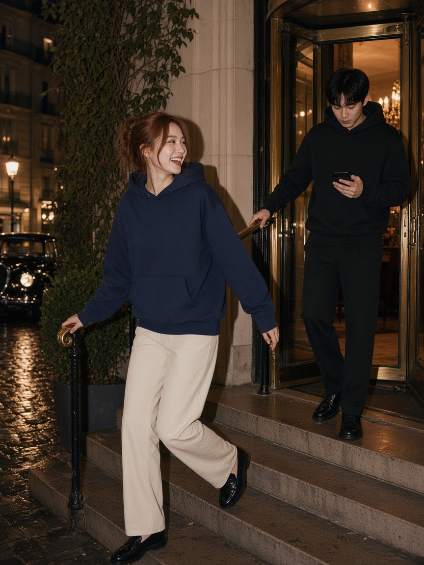 Man and woman in the Essential Heavyweight Pocket Hoodie in Black and Navy Blue on the side steps of a Paris grand hotel at night
