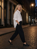 Woman in the Essential Jogged Sweatpants in Black with an oversized white poplin shirt and horsebit loafers, walking a cobbled SoHo street in New York at night
