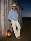 Man in the Essential Oversized Hoodie in Sky Blue with cream trousers and suede western boots, against a barn-wood wall at a ranch in Montana at blue hour
