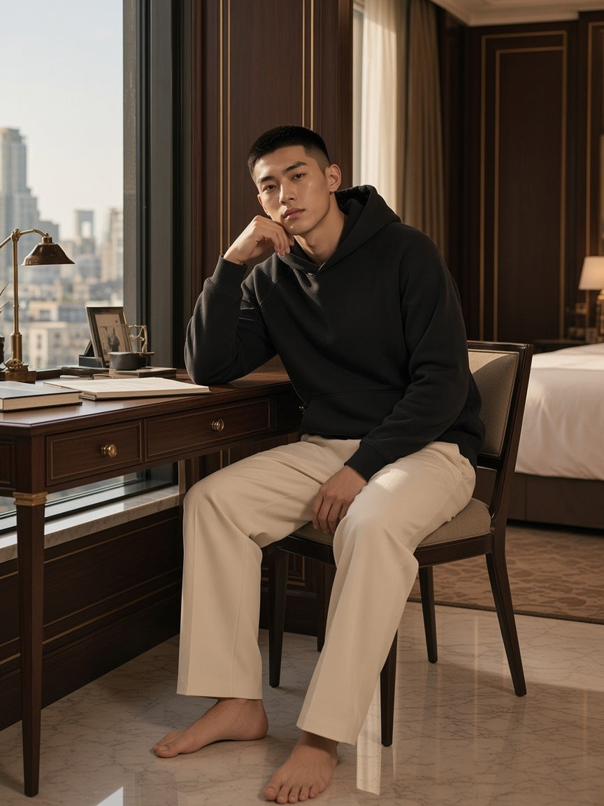 Man in the raglan-sleeve fleece hoodie in Black with cream tailored trousers, in an art-deco hotel suite in Shanghai by day