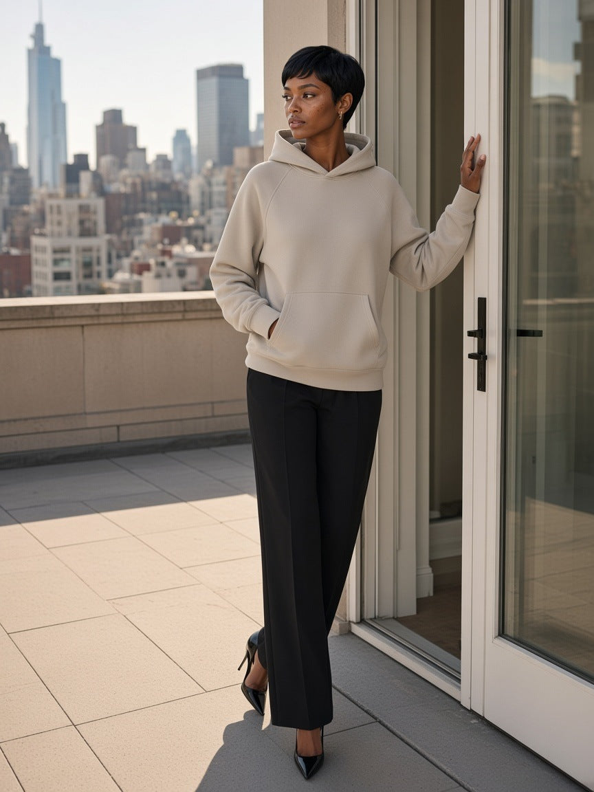Woman in the Essential Raglan Sleeve Fleece Hoodie in Oat Gray with black trousers and heels, walking a Park Avenue penthouse terrace in New York by day
