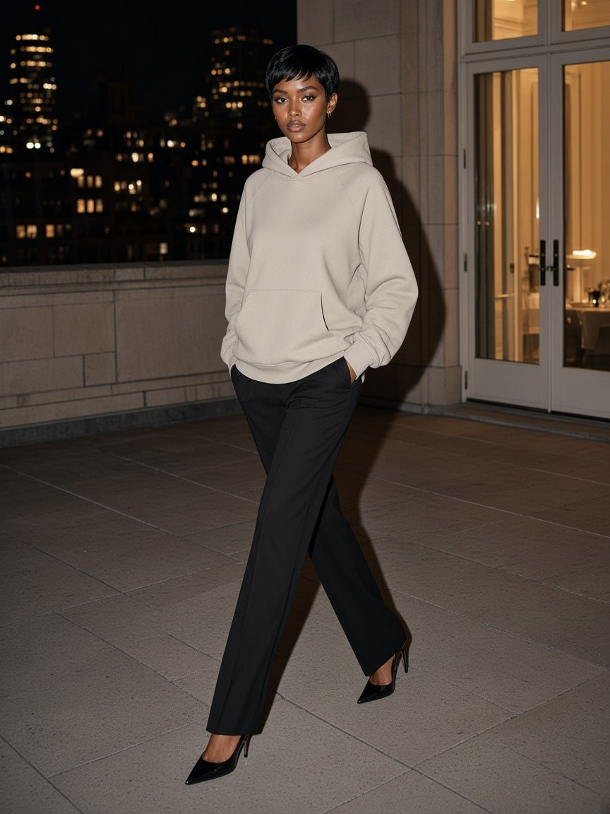 Woman in the Marcel Afters Essential Raglan Sleeve Fleece Hoodie in Oat Gray with black trousers and heels, walking a Park Avenue penthouse terrace in New York at night