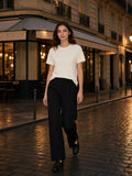 Woman in the Essential Standard Shoulder T-Shirt in Mild Apricot with black wide-leg trousers, walking a wet cobbled Paris street at night
