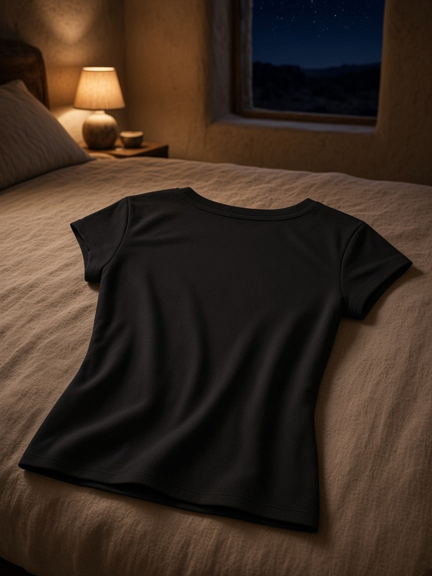 Essential V-Neck Bodycon T-Shirt in Black folded on a turned-down linen bed in a Marfa guesthouse at night