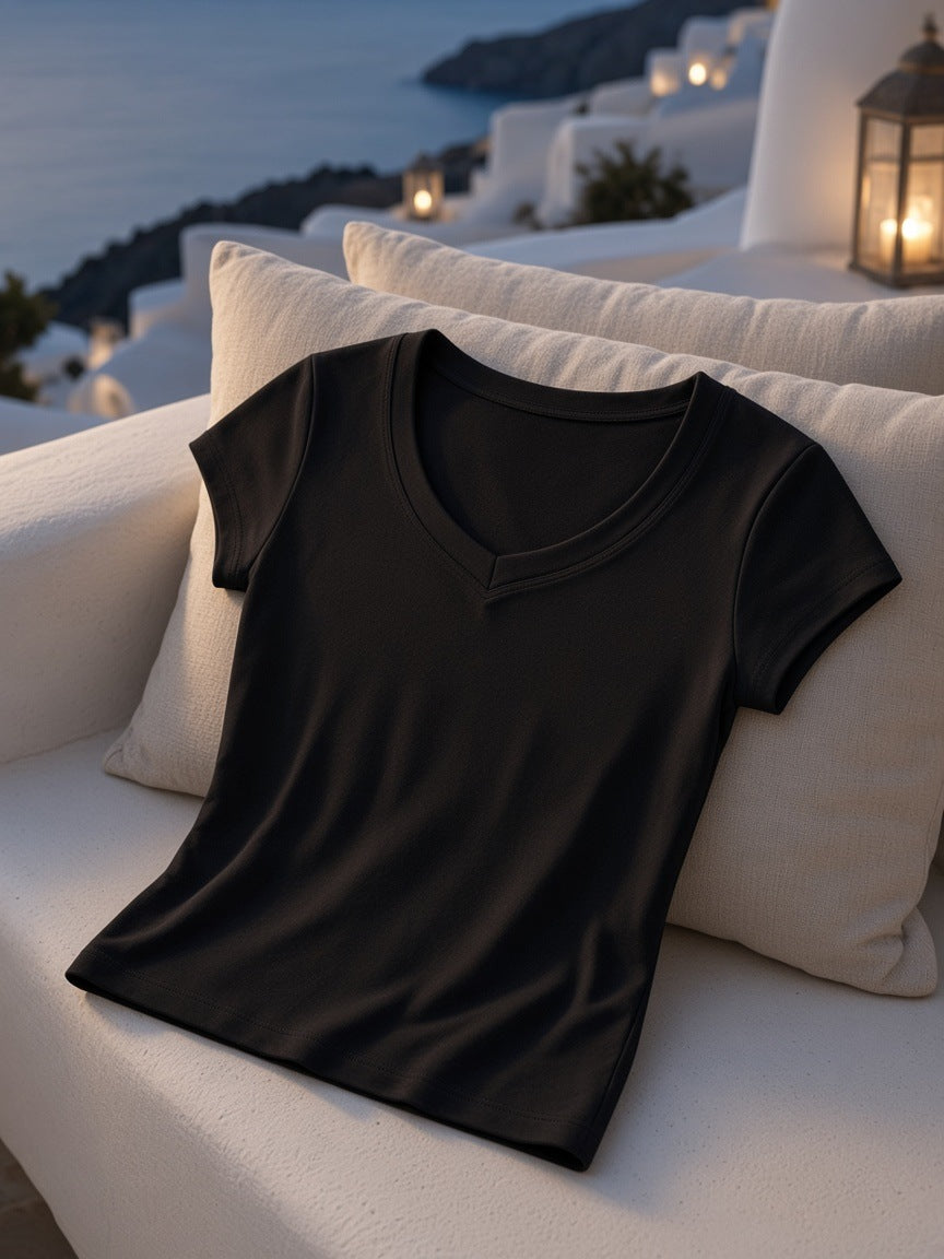Essential V-Neck Bodycon T-Shirt in Black folded on a built-in whitewashed bench with linen cushions in a Mykonos terrace suite at night