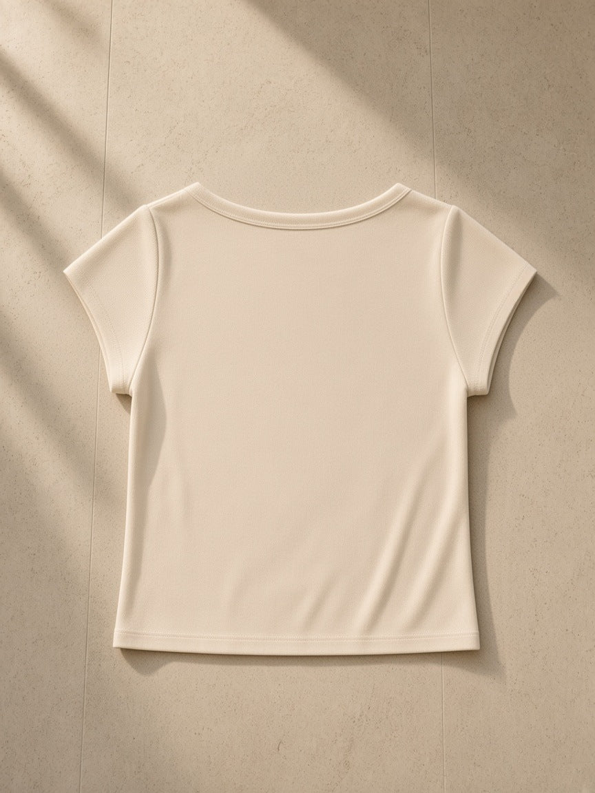Essential Wide Neck Baby T-shirt in Cream, laid flat on pale limestone, back view
