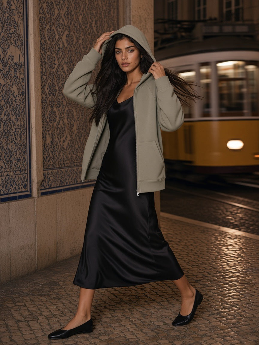 Woman in the zip-up fleece hoodie in Cement Gray over a black silk slip dress, at the Chiado tram stop in Lisbon at night