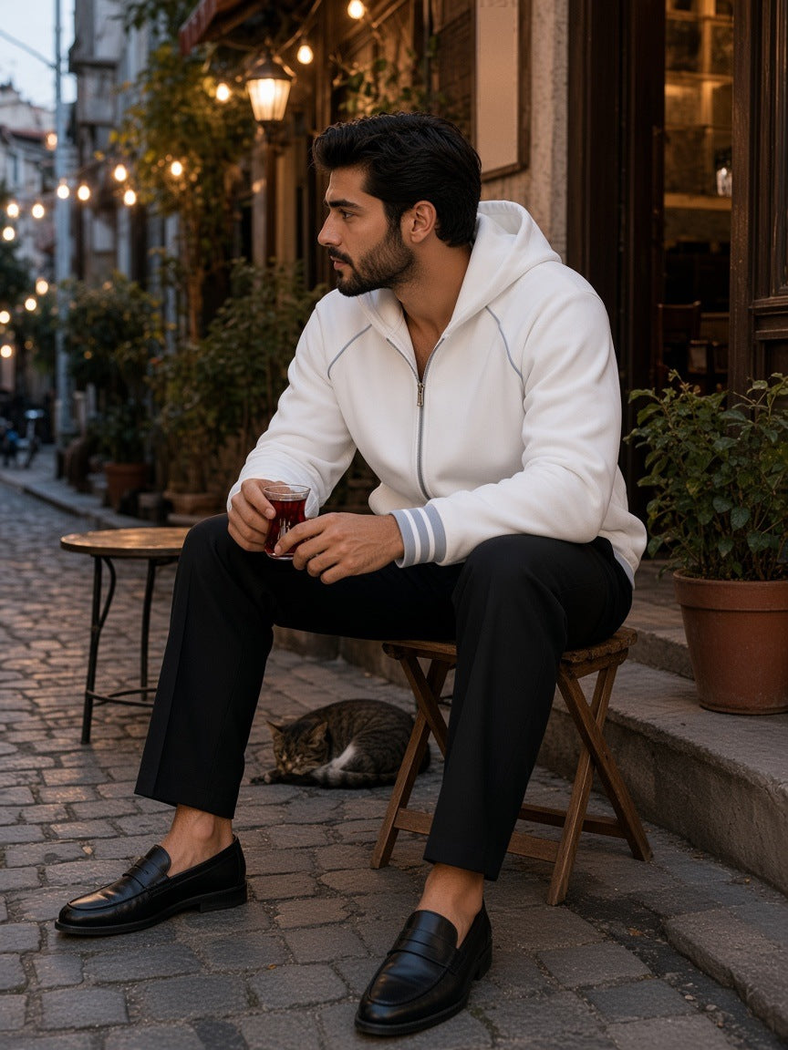Man in the Men's Striped Trim Zip-Up Hoodie in White with black trousers and loafers, holding a glass of tea outside an Istanbul tea house