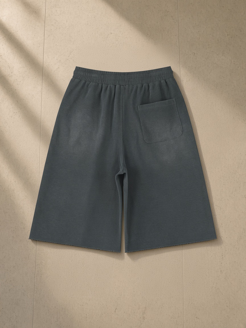 Unisex sunfade raw edge shorts in Gray, laid flat on pale limestone, back view