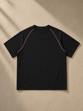 Unisex contrast stitch raglan t-shirt in Black, laid flat on pale limestone