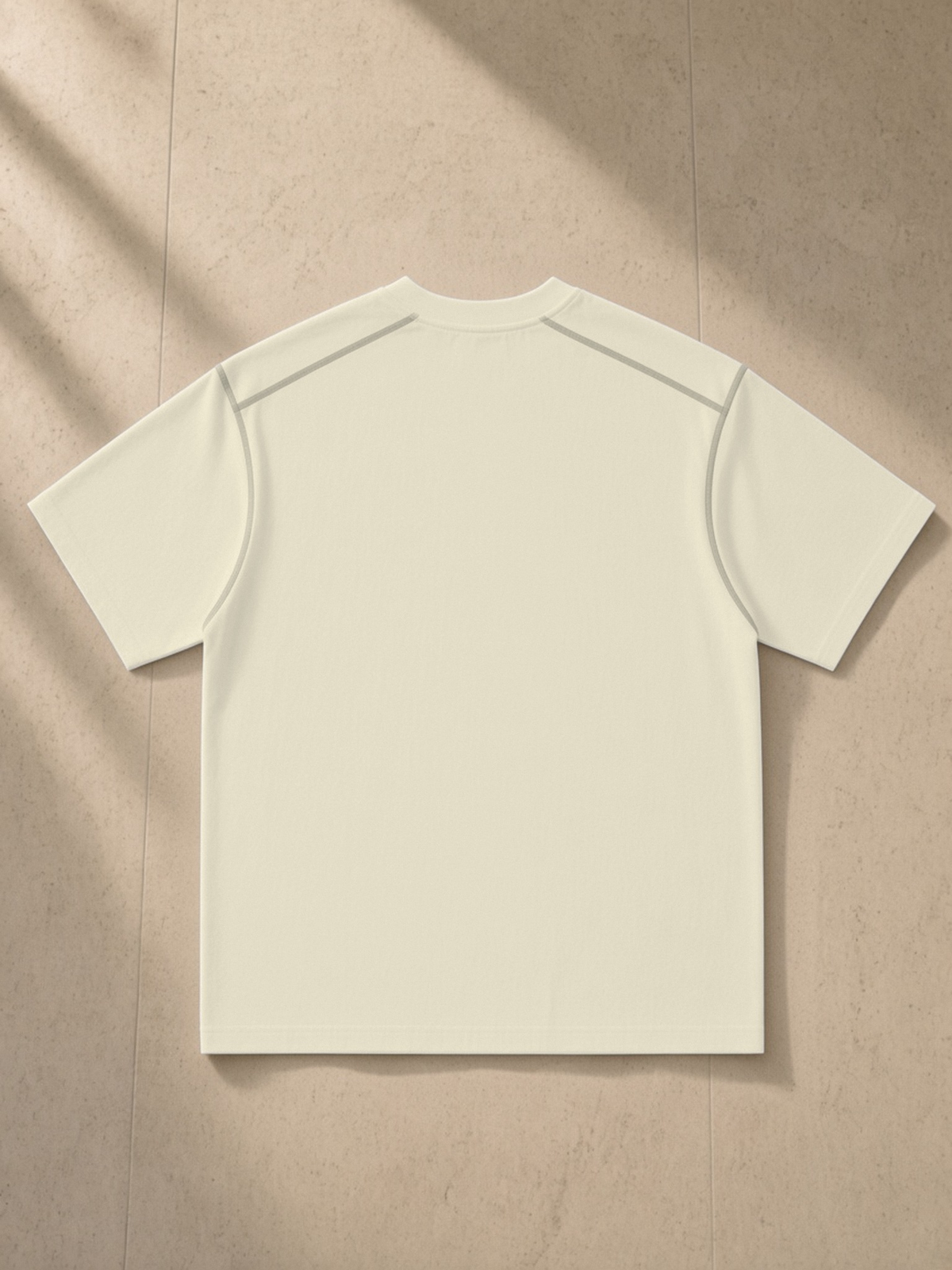 Oversized Contrast-Stitched Cotton Tee in Mild Apricot, laid flat on pale limestone, back.