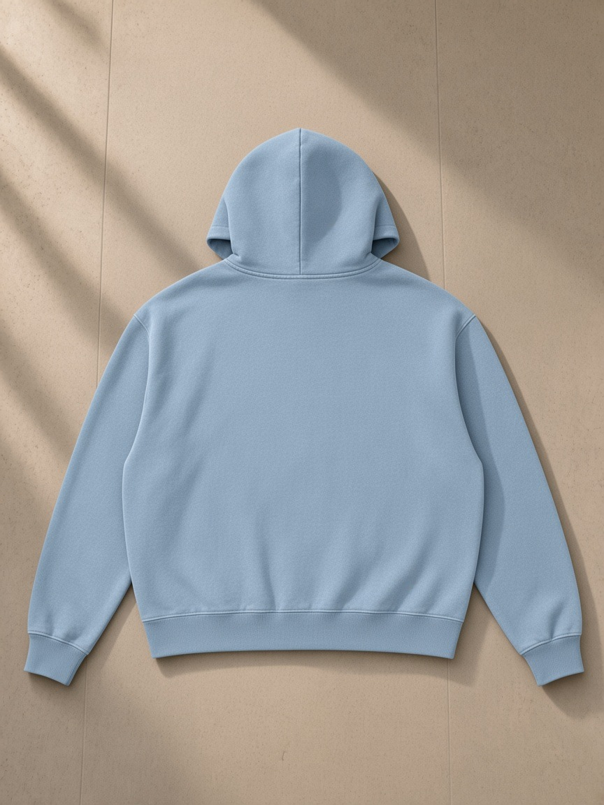 Mineral Wash Boxy Hoodie in Haze Blue, laid flat on pale limestone, back view