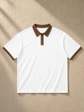 Unisex color block polo shirt in White with Brown, laid flat on pale limestone
