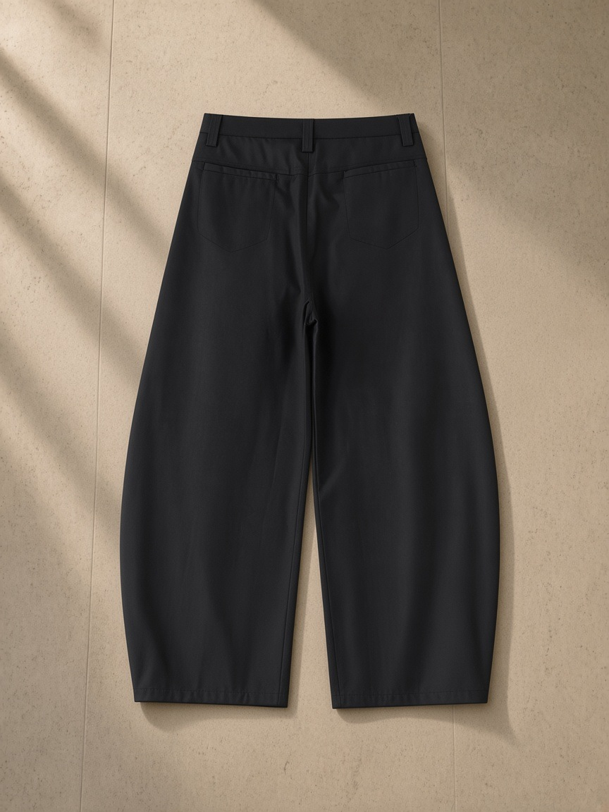 Essential Barrel Dress Pants in Black, laid flat on pale limestone, back view
