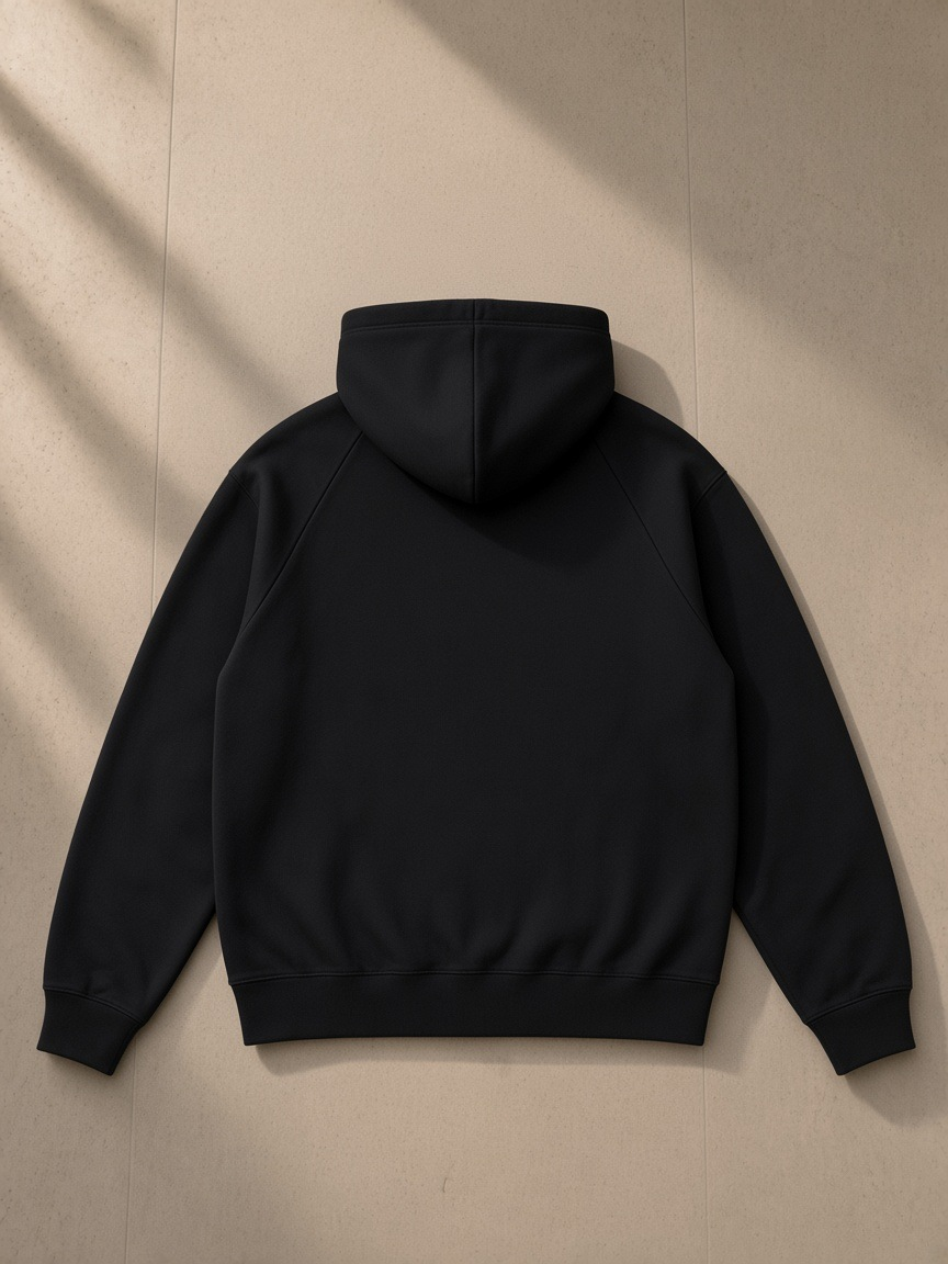 Unisex heavyweight raglan sleeve zip hoodie in Black, laid flat on pale limestone, back view