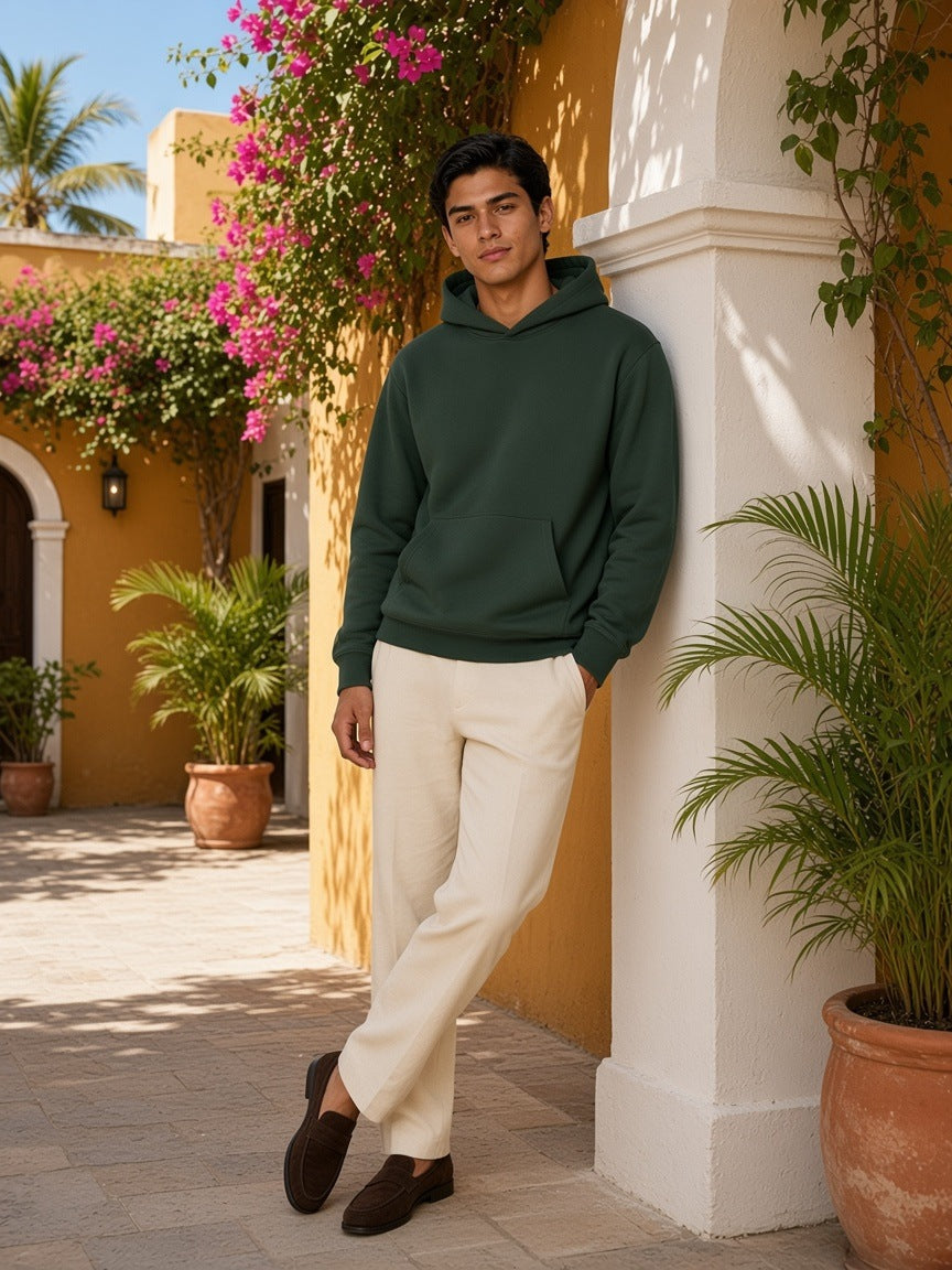 Man in the fleece regular shoulder hoodie in Dark Green with cream linen trousers, in a colonial hotel courtyard in Cartagena by day