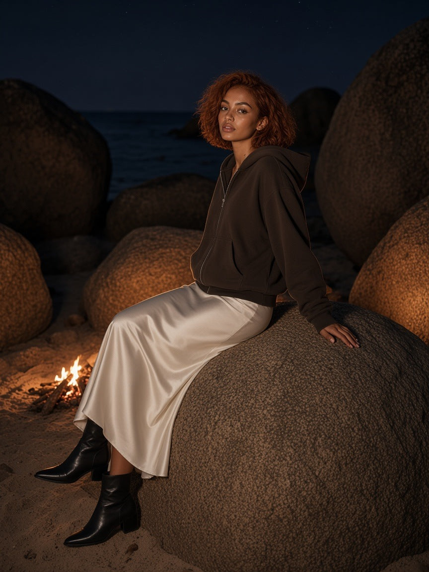Woman in the Marcel Afters fleece zip-up boxy hoodie in Brown with ivory wide-leg trousers, by a granite-boulder villa pool in the Seychelles at night