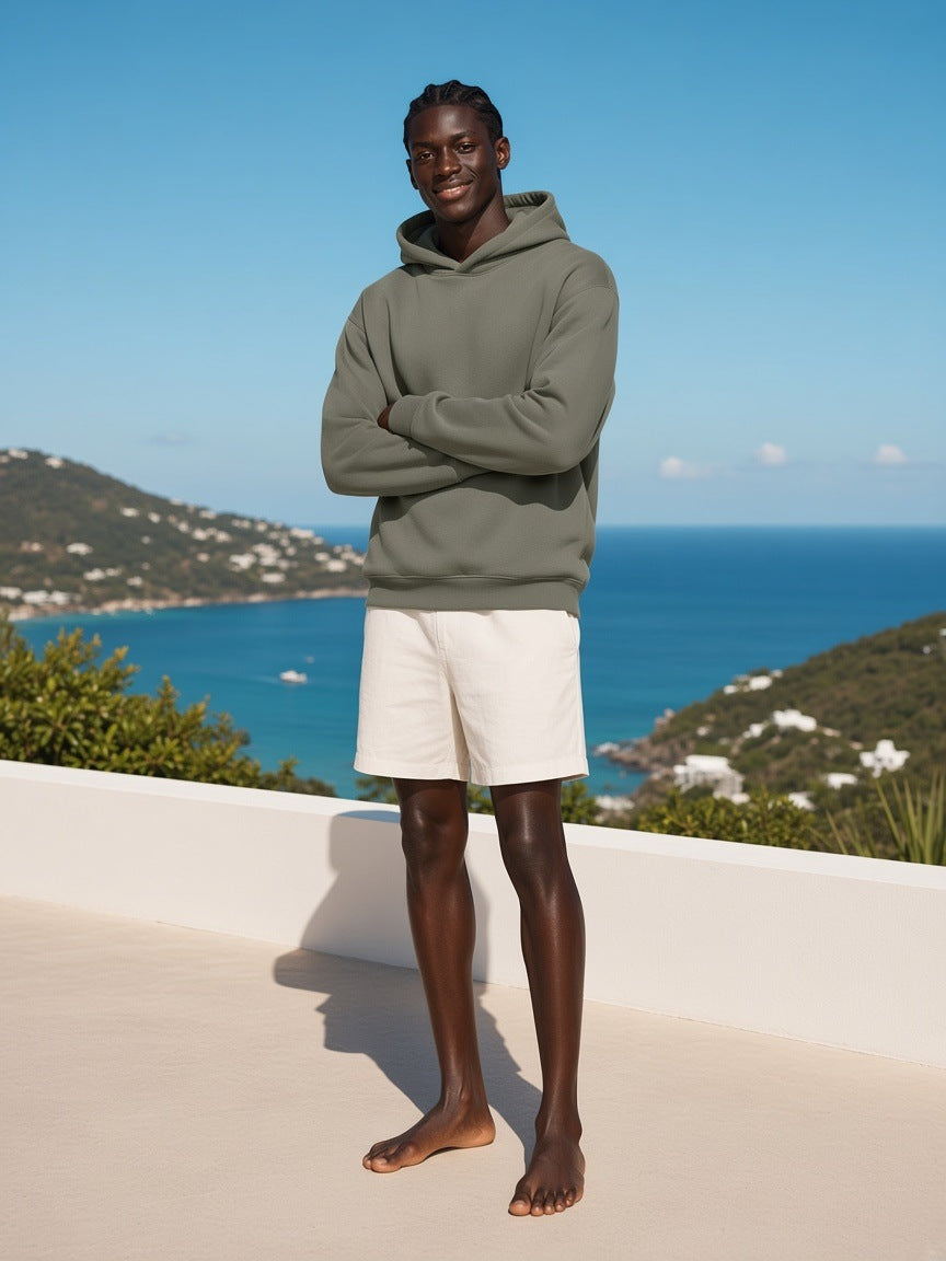 Man in the fleeced boxy hoodie in Dark Gray with ivory linen shorts, on a hillside villa terrace on Mustique in the morning