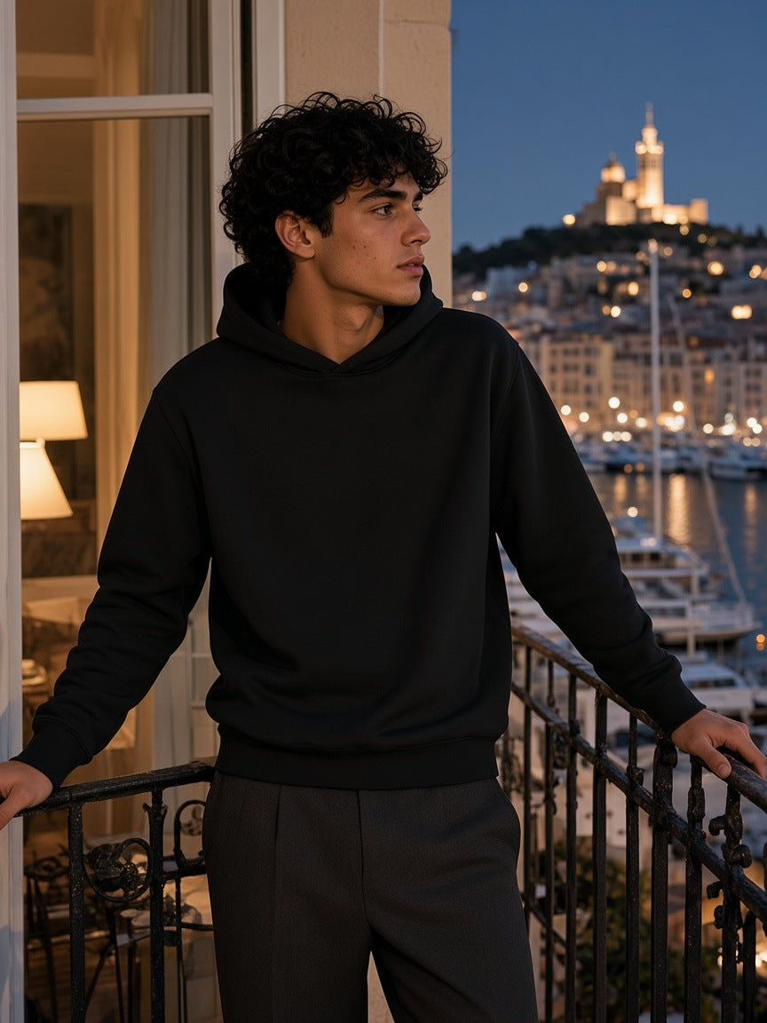 Man in the Marcel Afters Fleeced High Neck Hoodie in Black on a balcony above the Old Port of Marseille at night