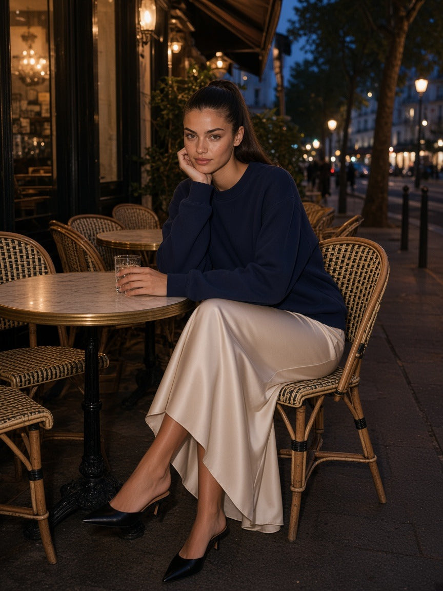 Woman in the Fleeced Sweatshirt in Navy Blue with an ivory satin slip skirt, at a café table on Place Dauphine in Paris at night