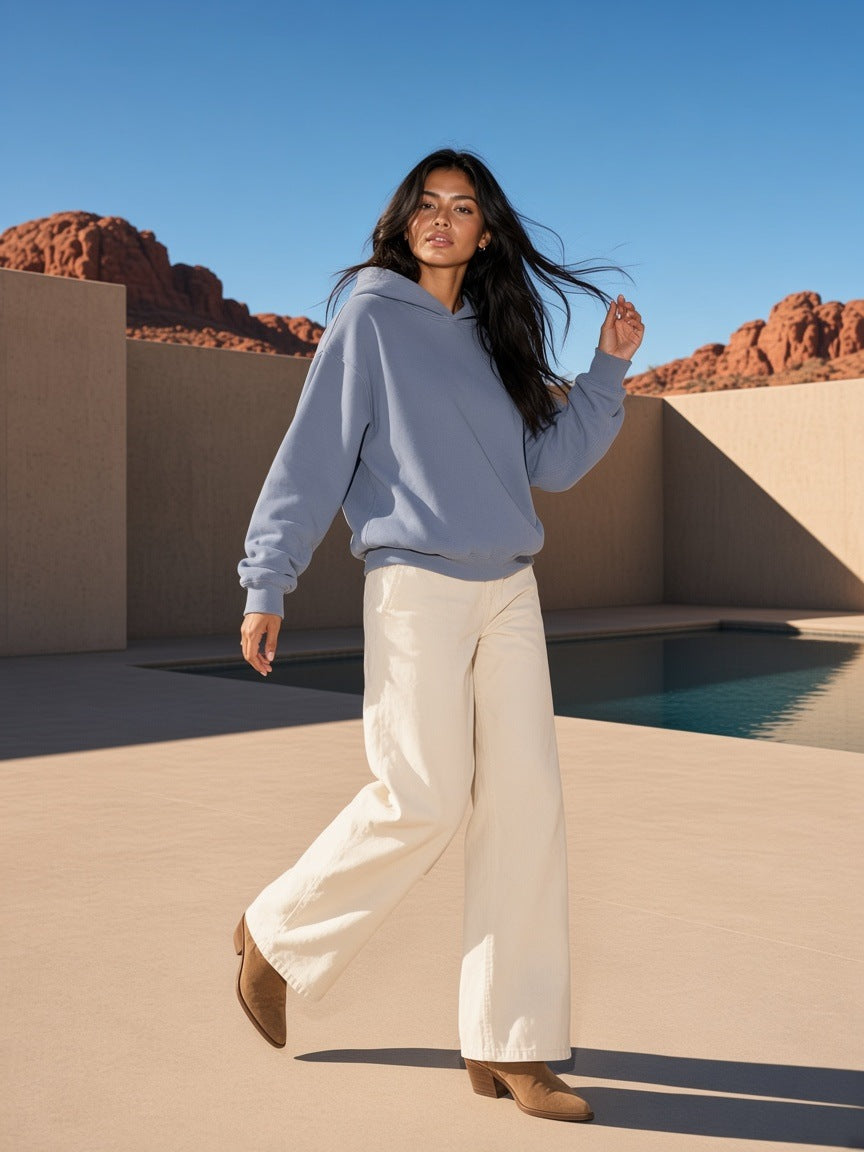 Woman in the Frayed Enzyme Washed Fleece Hoodie in Blue with cream trousers and suede boots, in a desert resort courtyard in Utah by day