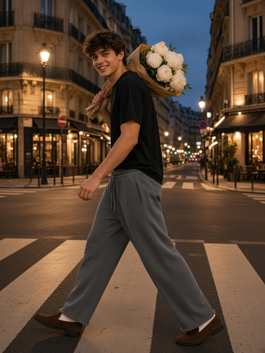 Man in the Frayed Enzyme Washed Fleece Sweatpants in Dark Gray crossing a Paris street at dusk with peonies over his shoulder