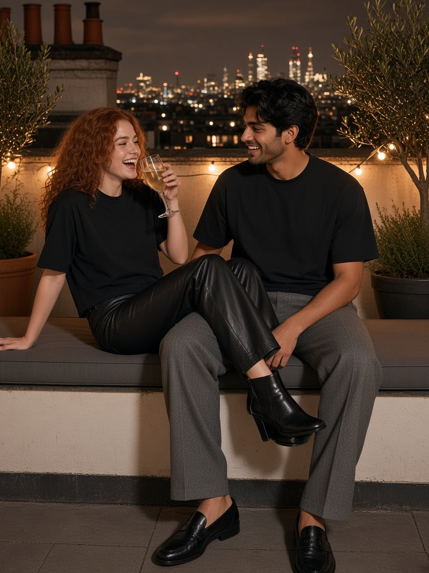 Marcel Afters French Terry Raw Edge T-Shirt in Black, worn by a man and a woman, seated on a rooftop lounge above the city at night in black raw-edge tees