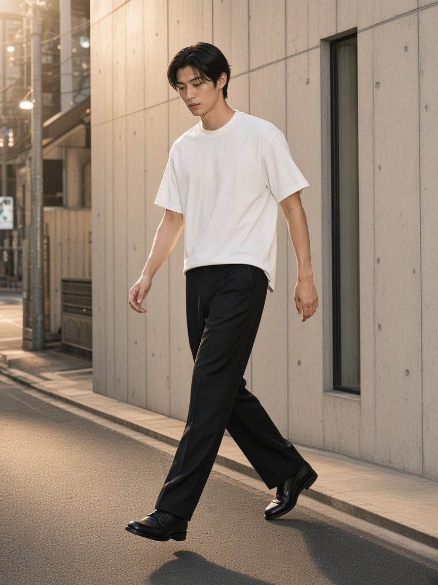 Man in the French Terry Raw Edge T-Shirt in White stepping off the kerb by a concrete facade in Aoyama, Tokyo in the morning