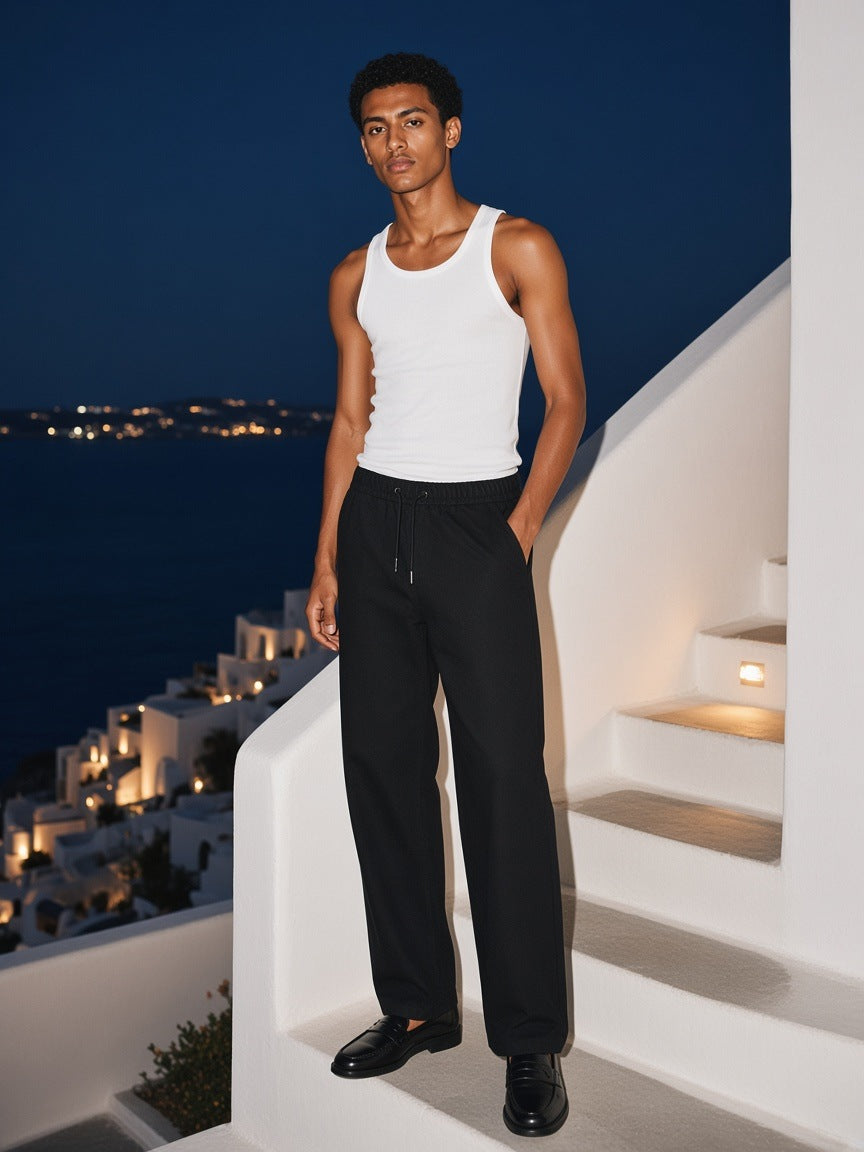 Man in the Heavyweight Cotton Straight-Leg Pants in Black standing on a whitewashed stair in Mykonos at night