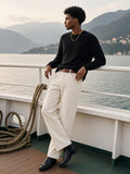 Man in the Heavyweight Cotton Straight-Leg Pants in Pale Khaki with a black knit, leather belt and Chelsea boots, leaning on the rail of a Lake Como ferry on a morning crossing