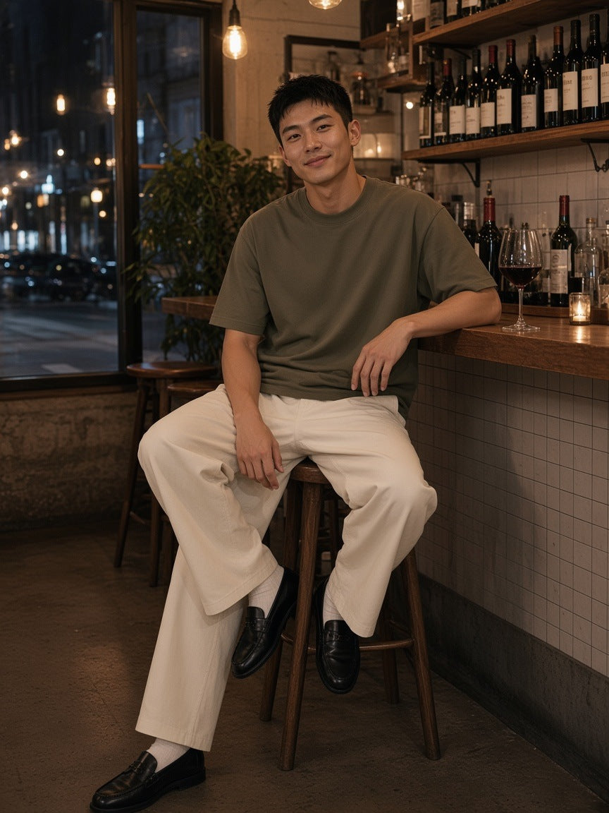 Man in the Marcel Afters heavyweight drop shoulder cotton t-shirt in Deep Khaki standing on a riverside terrace in Bangkok at night