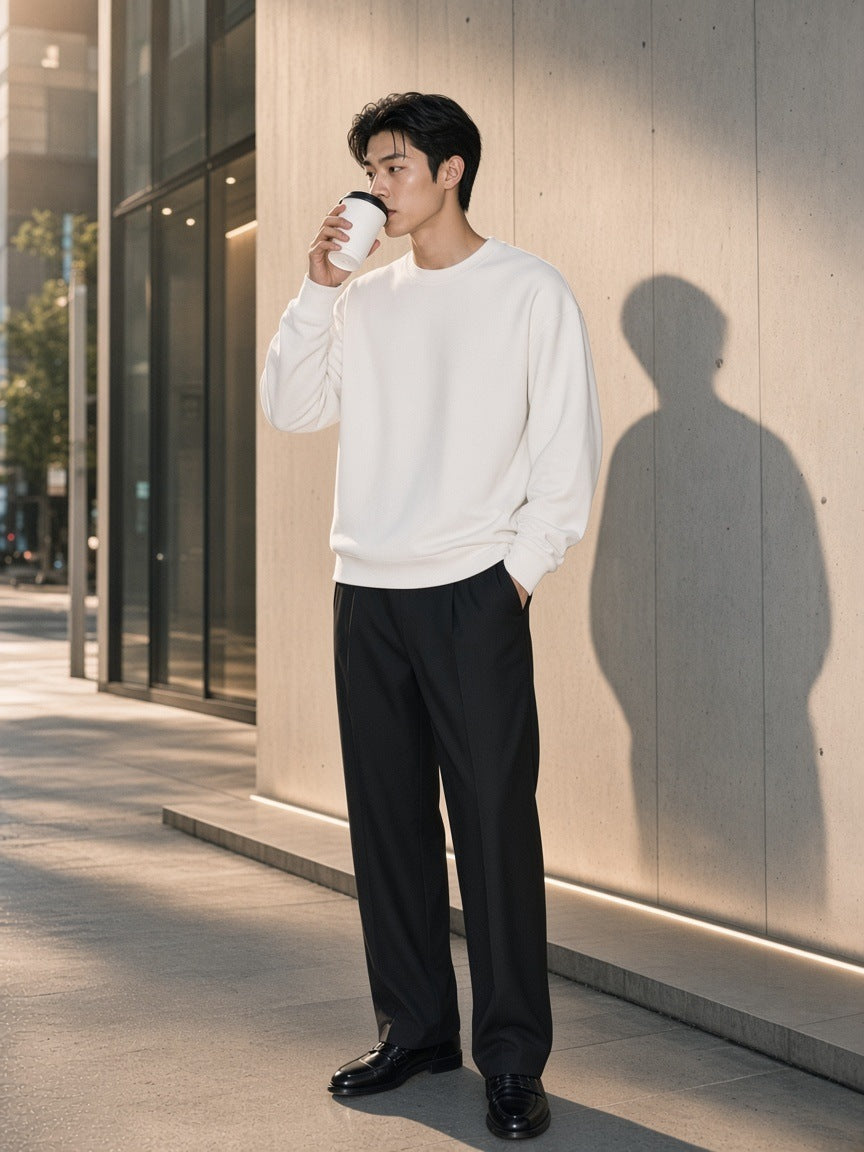 Man in the Heavyweight Drop Shoulder Sweatshirt in Lucent White with black pleated trousers and loafers, against raw concrete in Aoyama, Tokyo in the morning