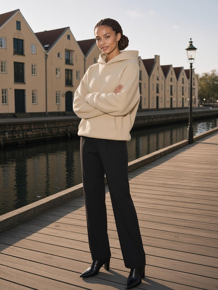 Woman in the Heavyweight Fleece Boxy Hoodie in Khaki with black trousers and ankle boots on the harbour boardwalk in Copenhagen in the morning