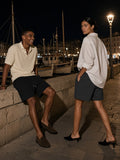 Two people in the Heavyweight Fleece Loose Fit Shorts in Black Beauty and Charcoal, one on a harbour wall and one walking past, at the Old Port of Marseille at night