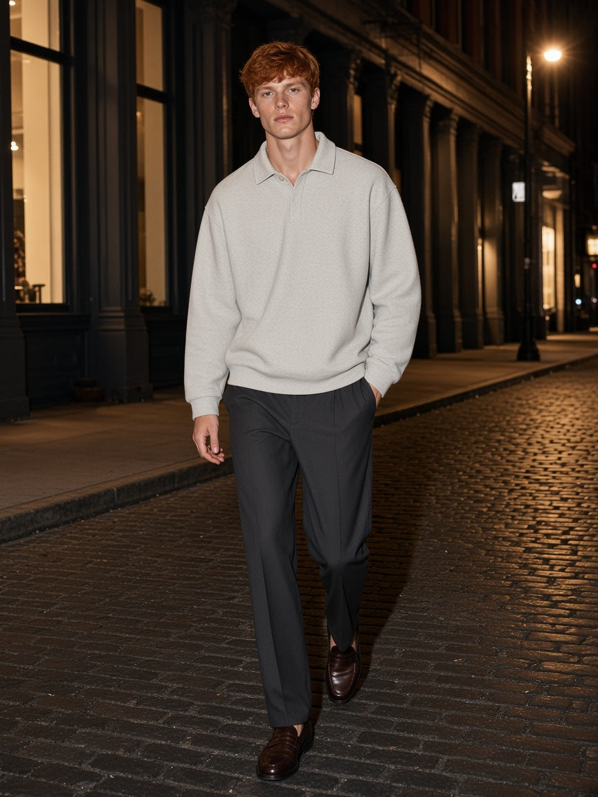 Man in the Marcel Afters Heavyweight Fleece Polo Sweatshirt in Oat Gray with charcoal trousers and loafers, walking a SoHo street in New York at night
