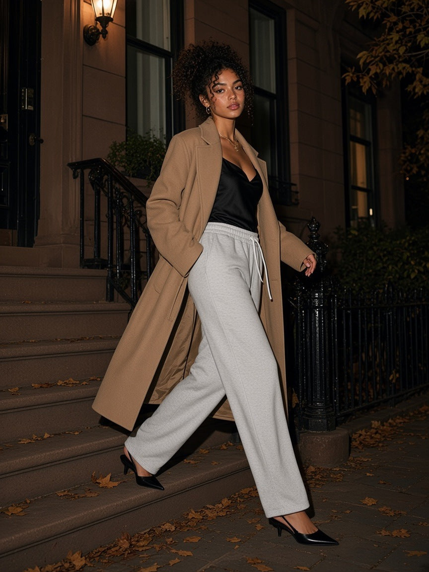 Woman in the Heavyweight Fleece Sweatpants in Flower Gray with a black silk cami, camel overcoat and pointed slingbacks, passing a Brooklyn brownstone stoop at midnight