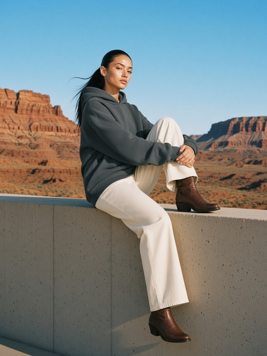 Woman in the heavyweight hidden pocket fleece hoodie in Charcoal sitting on a wall at a desert lodge in Utah in the morning