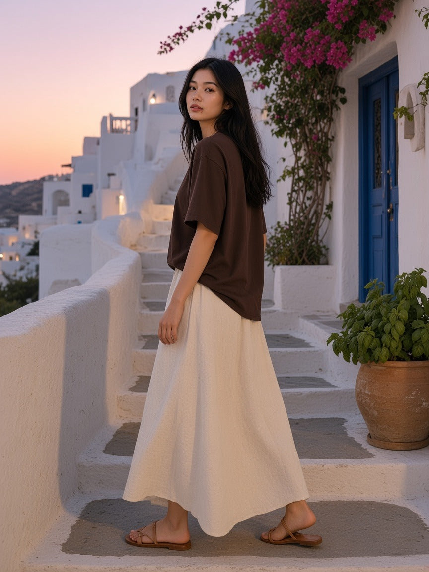 Marcel Afters Heavyweight Loose Fit T-Shirt in Brown, worn by a woman, walking whitewashed steps under bougainvillea in a brown boxy tee and cream skirt