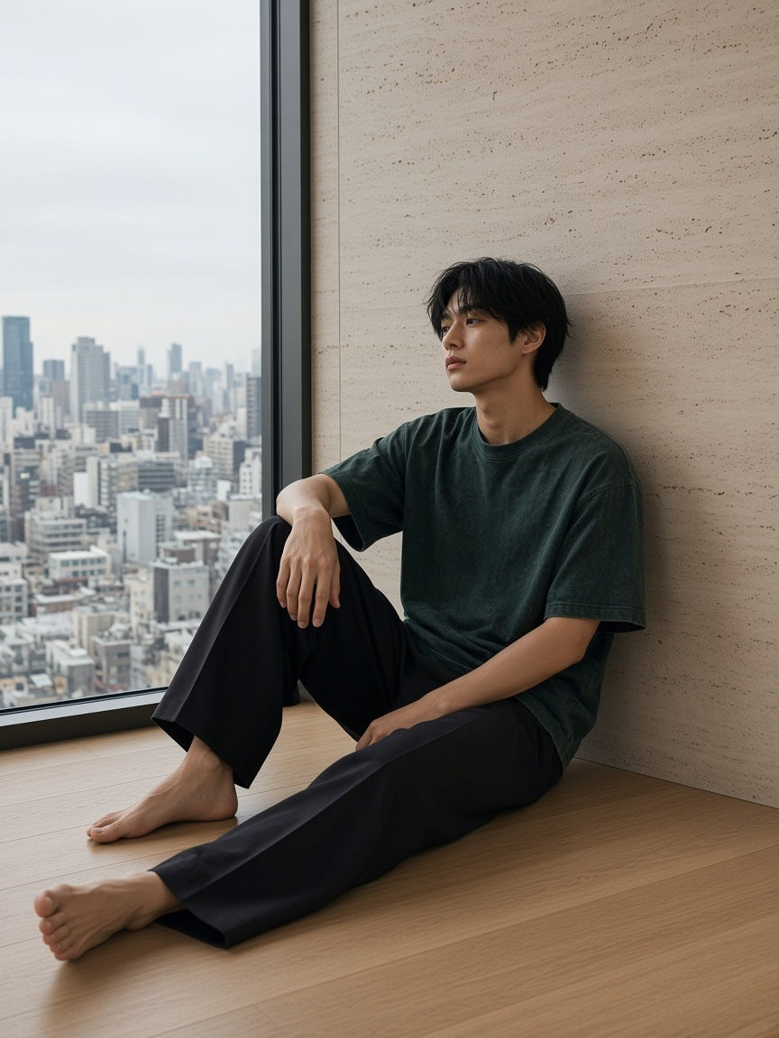 Man in the Men's Heavyweight Mineral Wash Boxy T-Shirt in Dark Green in a hotel suite above the city lights of Tokyo by day