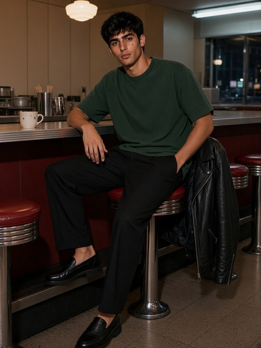 Man in the Men's Heavyweight Mineral Wash Boxy T-Shirt in Dark Green sitting at the counter of a Bowery diner in New York at night