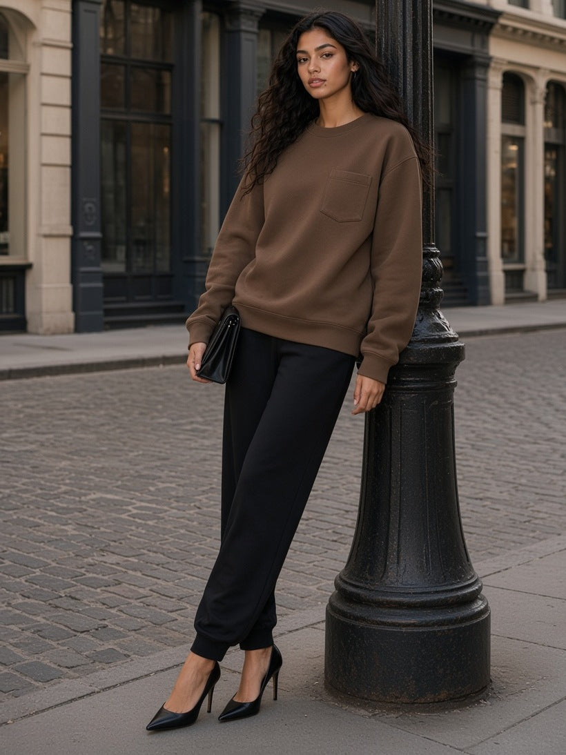 Woman in the Heavyweight Patch Pocket Crewneck Sweatshirt in Coffee with black joggers and heels, leaning on a cast-iron lamppost on a SoHo street in New York by day