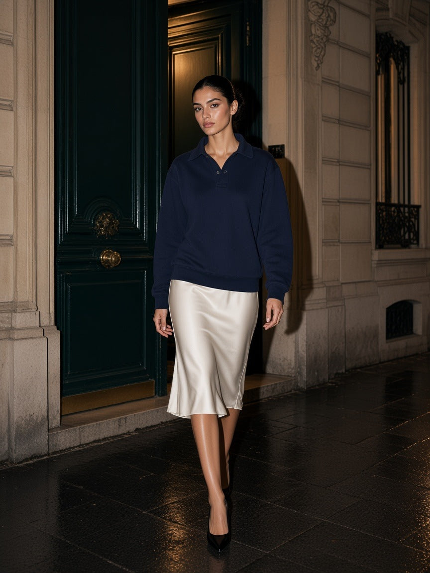 Woman in the Marcel Afters Heavyweight Polo-Collar Sweatshirt in Dark Blue with an ivory silk skirt and heels, stepping out of a Haussmann doorway in Paris at night