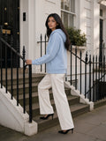 Woman in the Heavyweight Raglan Sleeve Zip Hoodie in Blue with white trousers and heels, on the front steps of a mews house in London in the morning