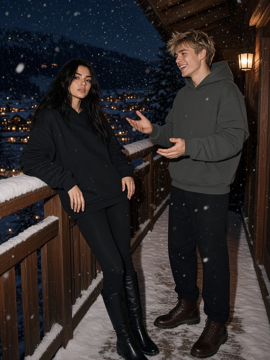 Marcel Afters Heavyweight Ruched Sleeves Hoodie in Black, worn by a man and a woman, talking on a snow-dusted chalet balcony at night in ruched-sleeve hoodies, one black and one dark grey