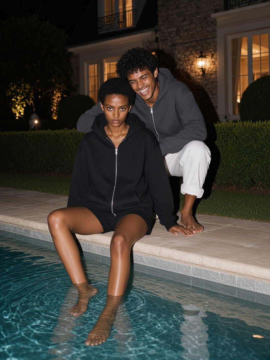 Two people in the Marcel Afters Heavyweight Zip-up Hoodie in Dark Gray and Black by a Hamptons estate pool at night