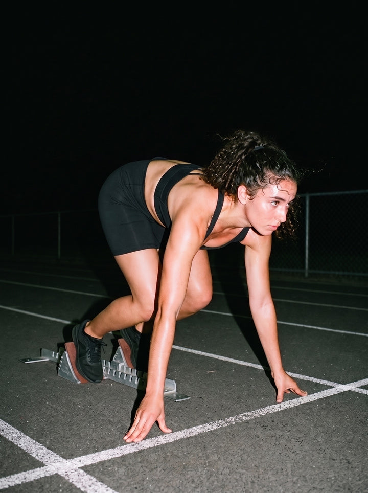 Woman in the High-Waisted Blend Biker Shorts in Black, in the starting blocks on a running track at night