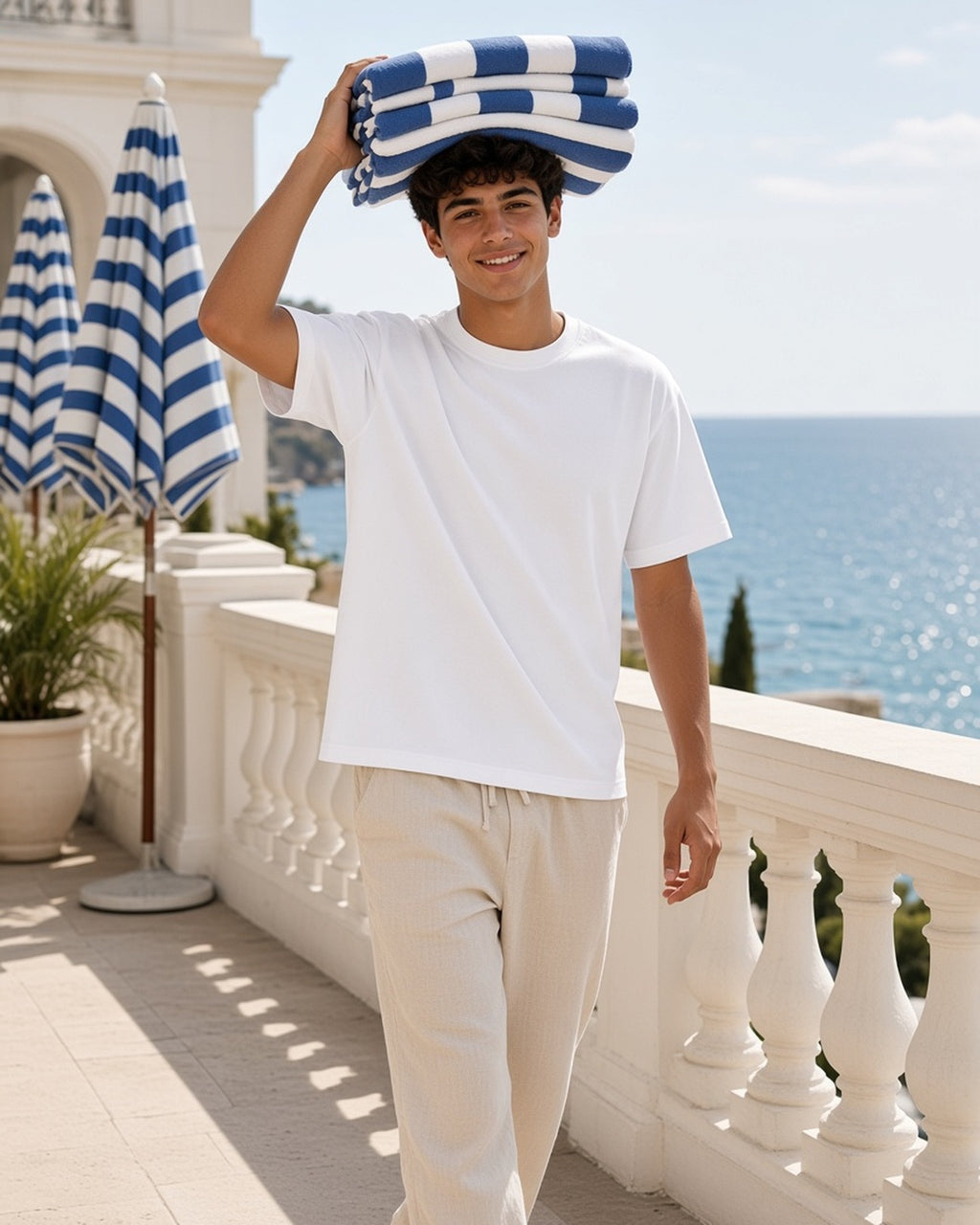 Man in the Heavyweight Mineral Wash Boxy T-Shirt in White, balancing folded beach towels on a Riviera hotel terrace