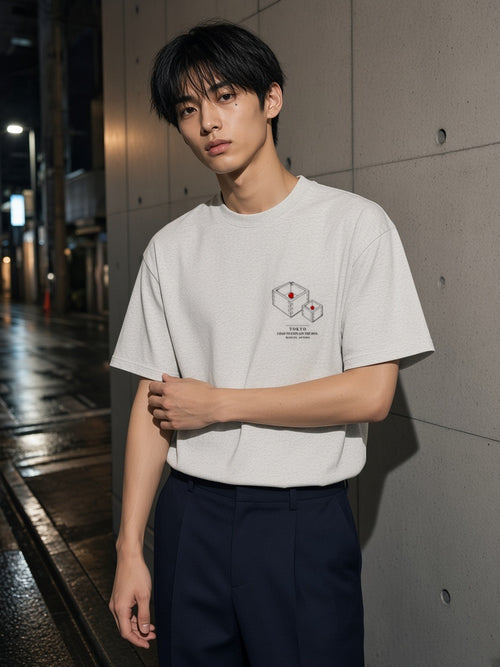 Man in the I Had To Explain The Box tee in Oat Gray against raw concrete in Aoyama, Tokyo at night