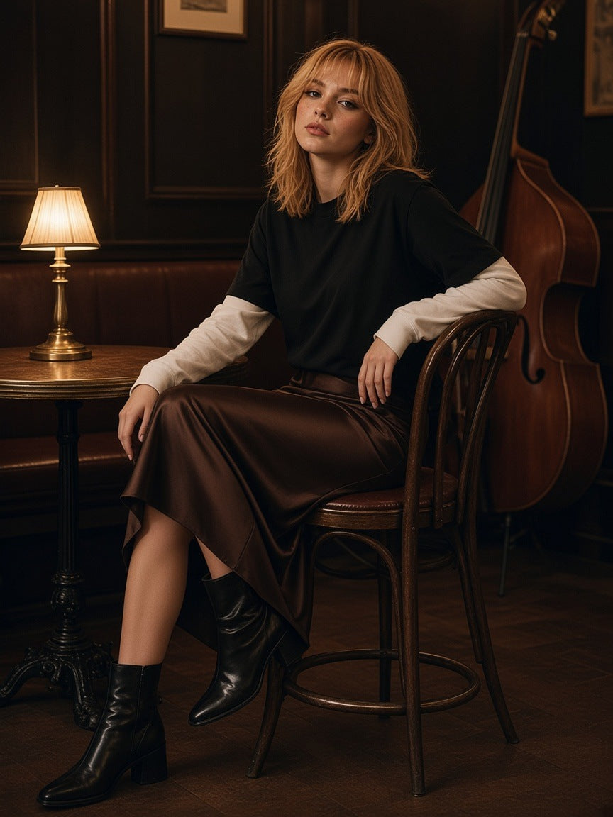 Woman in the Layered Contrast Sleeve Cotton T-Shirt in Black with White tucked into a chocolate satin midi with pointed ankle boots, perched on a bentwood chair in a jazz club at 1am